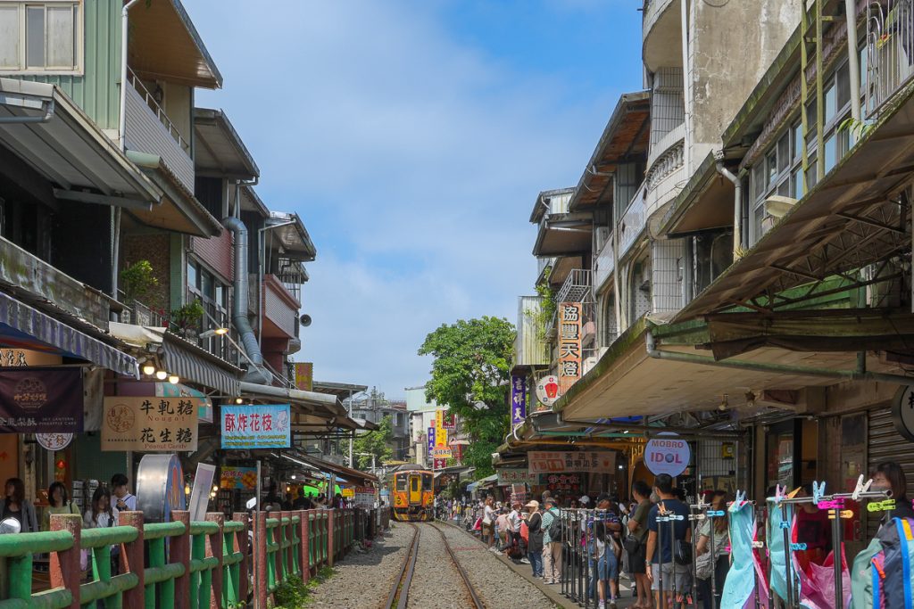 台湾・十分の街並み。線路沿いに立ち並ぶレトロな建物と、街の中をゆっくり走るローカル列車。線路と人々の暮らしが一体となった、十分らしい風景。